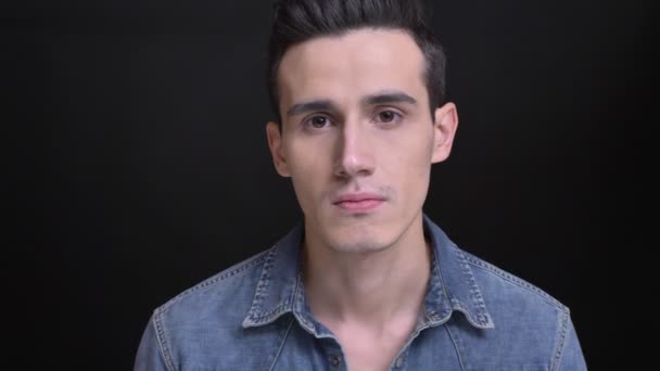 Närbild porträtt av unga kaukasiska manlig ansikte med bruna ögon tittar rakt på kameran med bakgrunden isolerade på svart — Stockvideo