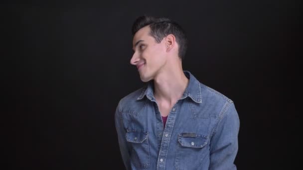 Closeup portret van de jonge Kaukasische leuke man worden verlegen en blij glimlachen en op zoek naar camera met de achtergrond geïsoleerd op zwart — Stockvideo