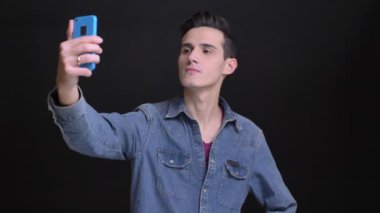 Portre portre Genç beyaz adam telefonda selfies alarak ve izole siyah arka plan ile resimleri görüntüleme