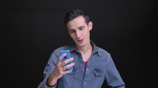 Крупним планом портрет молодого кавказького красивого чоловіка, що має відеодзвінок по телефону розмовляє і сміється випадково — стокове відео