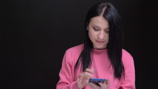Portretul de închidere al unei tinere femei caucaziene moderne care navighează pe telefon, uitându-se apoi la cameră zâmbind — Videoclip de stoc