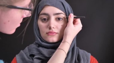 Kahverengi kalem ve fırça hijab siyah arka plan üzerine genç Müslüman kadın için makyaj yapıyor eller portresi.