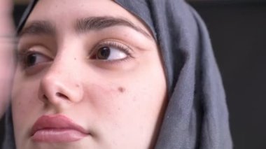 Yakın çekim portre profil kadın el kahverengi kalem ve fırça hijab siyah arka plan üzerine Müslüman kadın ile göz makyaj yapıyor.