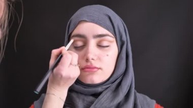 Genç Müslüman kadın için küçük fırça ile bir çizgi Hicap siyah arka plan üzerine çekerek göz makyaj yaparken eller portresi.