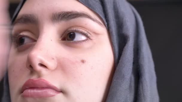 Close-up portret in profiel van vrouwelijke handen doen oog make-up met bruin potlood en penseel voor Moslimvrouw in hijab op zwarte achtergrond. — Stockvideo