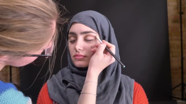 Potret tangan perempuan melakukan make-up mata dengan pensil coklat dan sikat untuk wanita muslim yang cantik berhijab dengan latar belakang hitam . — Stok Video