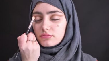 Hijab güzel Müslüman kadın için fırça ile siyah arka plan üzerine stumping göz makyaj yaparken eller portresi.