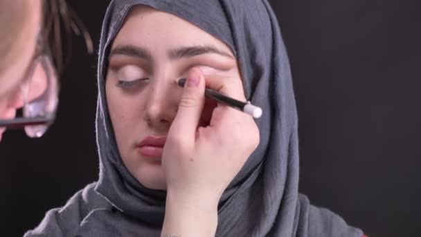 Portrait of female hands doing eye-makeup with white pencil for beautiful muslim woman in hijab on black background. — Stock Video