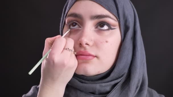 얇은 평면 브러쉬를 사용 하 여 매력적인 무슬림 여성 hijab 검은 배경에 검은 화살표 그리기 여성 손의 초상화. — 비디오