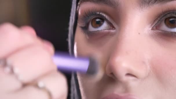 Close-up retrato de mãos femininas fazendo maquiagem e colocando a base para a bela mulher muçulmana no hijab no fundo preto . — Vídeo de Stock