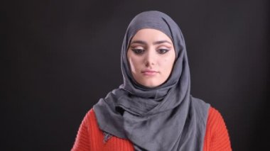 Sakin bir şekilde içine kamera siyah arka plan üzerine izlerken parlak makyajlı hijab güzel Müslüman kadın portresi.