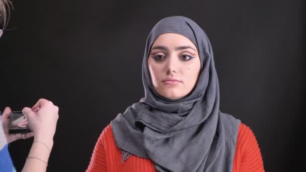 黒い背景にヒジャーブの魅力的なイスラム教徒の女性の顔にフラット ブラシで蛍光ペンに入れてガラスのメイクアップ アーティストの肖像画. — ストック動画