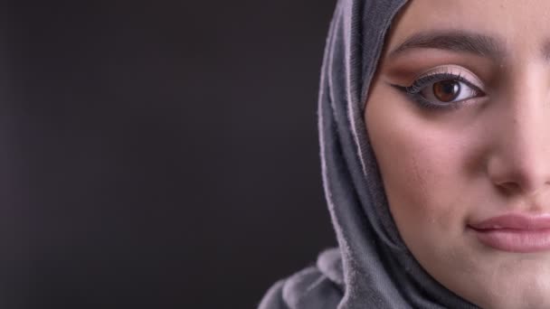 Close-up half-portrait of young muslim woman in hijab with fashionable make-up watching calmly into camera on black background. — Stock Video