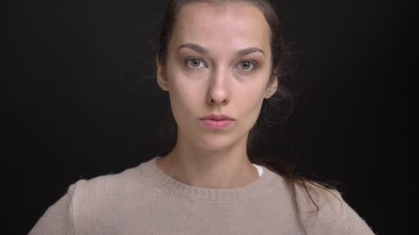 Close-up portret van jonge brunette Kaukasische meisje met paardenstaart serieus kijken naar de camera op zwarte achtergrond. — Stockvideo