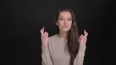 Uzun saçlı esmer kız sevinçle el parmak çarpı işareti işareti umut kamera içine siyah arka plan üzerine göstermek için portresi.