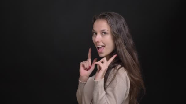 Detailní portrét brunetka dlouhé vlasy-kavkazský dívky s úsměvem, aby zbraň znamení do kamery na černém pozadí. — Stock video