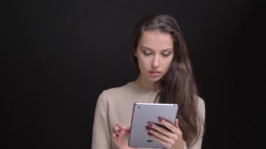 Genç esmer uzun saçlı beyaz kız gülümseyerek tablet siyah arka plan üzerinde içine izlerken portresi.