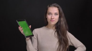 Genç esmer uzun saçlı beyaz kız gülümseyerek içine kamera siyah zemin üzerine yeşil ekran tablet gösterilen portresi.