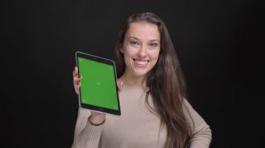 Genç esmer uzun saçlı beyaz kız mutlu bir şekilde içine kamera siyah zemin üzerine yeşil ekran tablet gösterilen portresi.