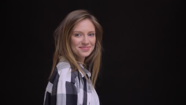 Portrait in profile of young caucasian long-haired girl in plaid shirt turns to camera and watches joyfully into it on black background. — Stock Video