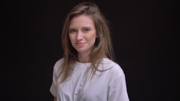 Retrato en el perfil de la joven caucásica de pelo largo chica en blanco camiseta relojes sonriendo en la cámara sobre fondo negro . — Vídeos de Stock