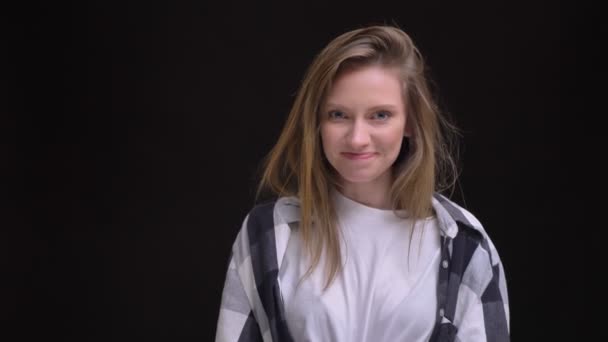 Retrato de alegre jovem caucasiano de cabelos compridos menina em camisa xadrez humildemente sorrindo para a câmera no fundo preto . — Vídeo de Stock
