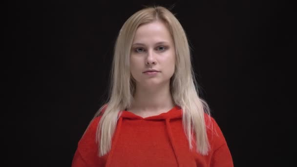 年轻的白发白种人女孩的肖像在红色毛衣平静地观看在黑色背景的照相机 — 图库视频影像