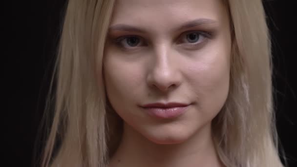 Närbild porträtt av unga vithårig kaukasiska flicka i röd tröja tittar lugnt in kameran på svart bakgrund. — Stockvideo
