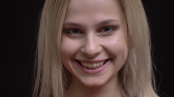 Retrato de cerca de una joven caucásica de pelo blanco en suéter rojo mirando sonriente a la cámara sobre fondo negro . — Vídeos de Stock