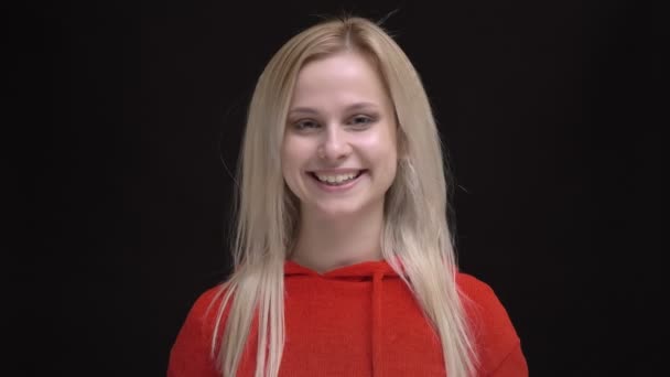 Retrato de una joven caucásica de pelo blanco en suéter rojo sacudiendo el pelo y sonriendo humildemente en la cámara sobre fondo negro . — Vídeos de Stock