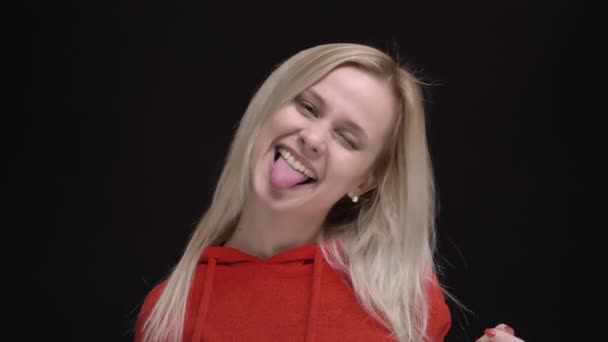 Portrait of young white-haired caucasian girl in red sweater joyfully making funny faces into camera on black background. — Stock Video