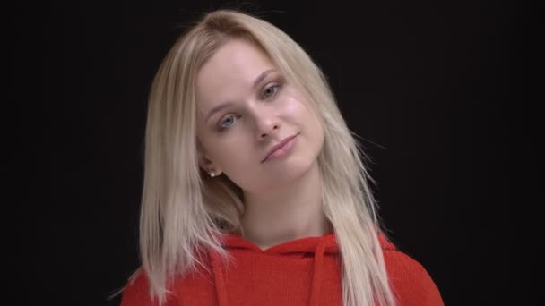 Portrait of young white-haired caucasian girl in red sweater thoughtfully watching into camera on black background. — Stock Video