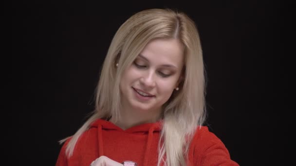 Retrato de una joven caucásica de pelo blanco en suéter rojo mirando los relojes y sintiéndose aburrida de esperar sobre fondo negro . — Vídeo de stock