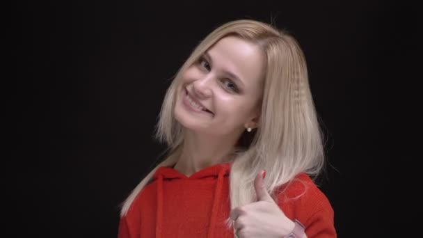 Retrato de cabelos brancos menina caucasiana em suéter vermelho gestual sinal de dedo para cima para mostrar como e respeito no fundo preto . — Vídeo de Stock