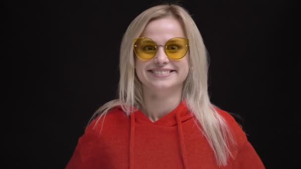 Portrait of young white-haired caucasian girl in yellow sunglasses happily jumping on black background. — Stock Video