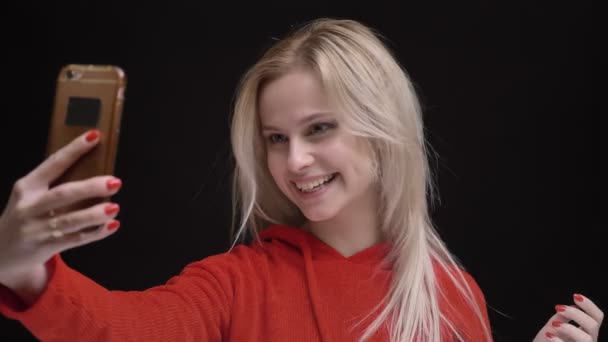 Jong wit-haired Kaukasische meisje in gele zonnebril glimlachend selfie-foto's maken met behulp van smartphone op zwarte achtergrond. — Stockvideo