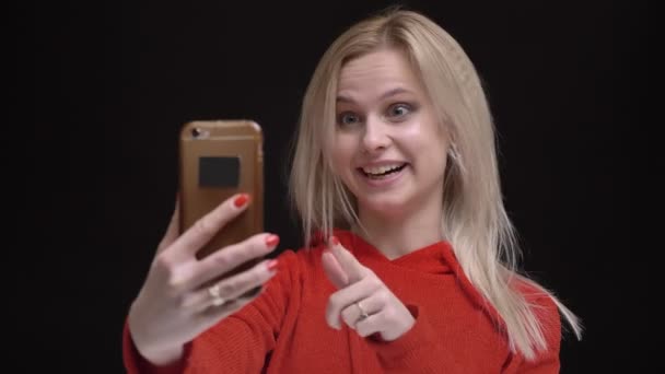 Jong wit-haired Kaukasische meisje in gele zonnebril glimlachend praten in videochat op smartphone op zwarte achtergrond. — Stockvideo