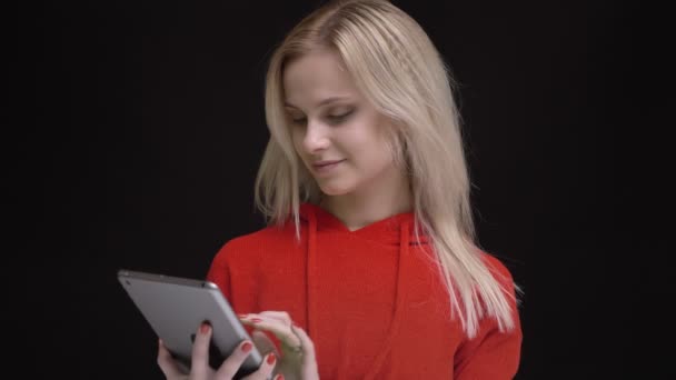 Joven chica caucásica de pelo blanco en suéter rojo que sonríe mostrando la pantalla verde de la tableta y el signo de dedo en el fondo negro . — Vídeos de Stock