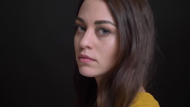 Primer plano retrato de chica morena de pelo largo en suéter amarillo se convierte en cámara y mira seriamente sobre fondo negro . — Vídeos de Stock