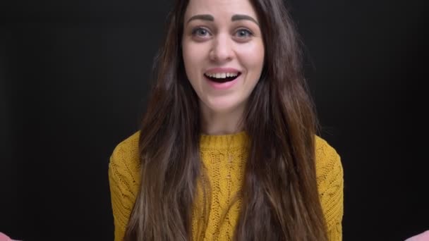 Porträt eines langhaarigen brünetten Mädchens im gelben Pullover, das vor der Kamera positive Belustigung und Glück auf schwarzem Hintergrund zeigt. — Stockvideo