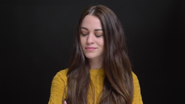 Portret van langharige brunette Kaukasische meisje in gele trui met gekruiste armen serieus kijken naar de camera op zwarte achtergrond. — Stockvideo