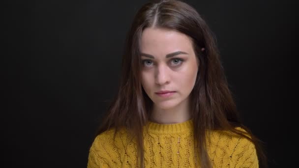 Портрет молодої довгошерстої брюнетки білої дівчини в жовтому светрі, який на жаль дивиться в камеру на чорному тлі . — стокове відео