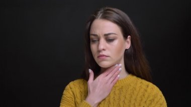 Siyah arka plan üzerine öksürük ve boğaz ağrısı sahip sarı kazaklı genç uzun saçlı esmer beyaz kız portresi.