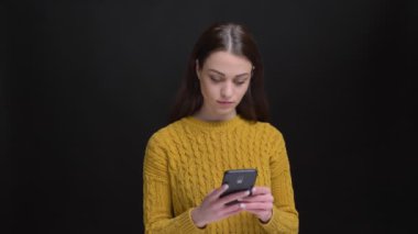 Sarı kazaklı gülümseyerek smartphone ile siyah arka plan üzerine çalışma uzun saçlı esmer kız portresi.