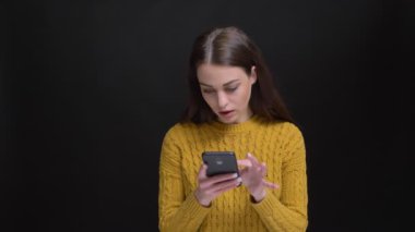 Sarı kazaklı dikkatle smartphone ile siyah arka plan üzerine çalışma uzun saçlı esmer kız portresi.