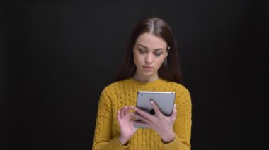 Dikkatle tablet ile çalışma ve siyah arka plan üzerine kamera içine izlerken sarı kazaklı uzun saçlı esmer kız portresi.