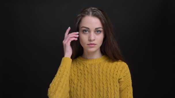 Portret van langharige brunette meisje in gele trui fashionably poseren in camera op zwarte achtergrond. — Stockvideo