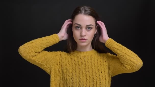 Retrato de chica morena de pelo largo en suéter amarillo fijando su cabello y posando a la moda en la cámara sobre fondo negro . — Vídeos de Stock
