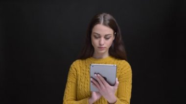 Dikkatle tablet ile çalışma ve içine kamera siyah arka plan üzerine gülen sarı kazaklı uzun saçlı esmer kız portresi.