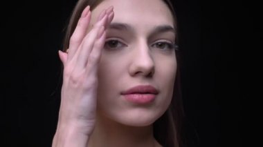 Yakın çekim portre genç beyaz kızın çıplak makyaj yumuşak yüzünü siyah arka plan üzerine dokunmadan kamera içine izlerken ile.